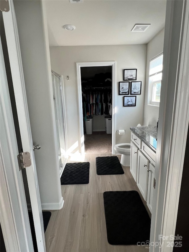 bathroom featuring a stall shower, visible vents, toilet, wood finished floors, and vanity