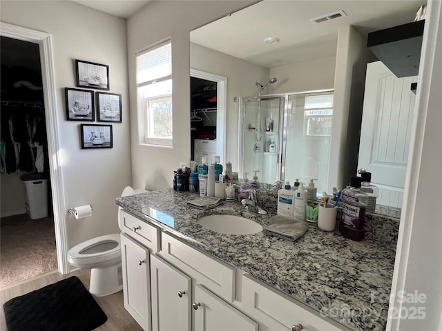 bathroom featuring visible vents, wood finished floors, a walk in closet, vanity, and a shower stall