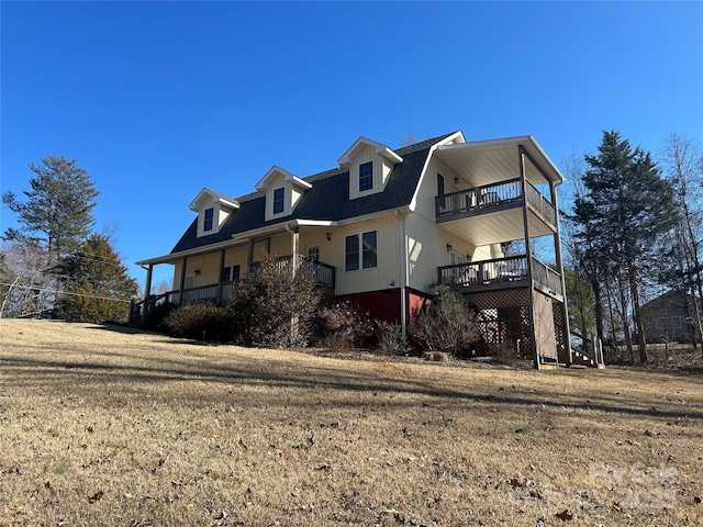 view of front facade featuring a shingled roof, a front yard, and a balcony