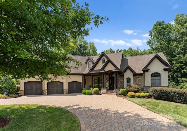 view of front of property featuring a garage, stone siding, decorative driveway, stucco siding, and a front yard