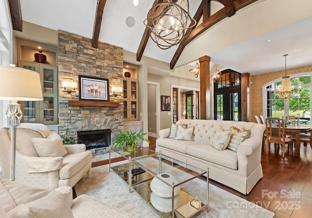 living area with lofted ceiling with beams, wood finished floors, built in shelves, a chandelier, and a fireplace