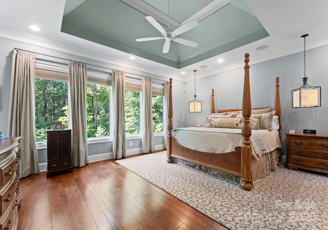 bedroom with crown molding, a tray ceiling, wood finished floors, and recessed lighting