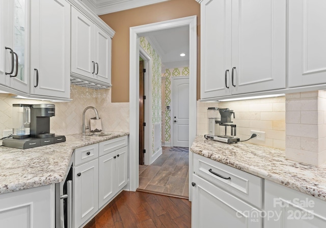 kitchen with a sink, white cabinetry, ornamental molding, light stone countertops, and dark wood-style floors