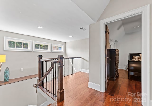 hallway with dark wood-type flooring, a wealth of natural light, visible vents, and an upstairs landing