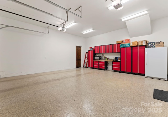 garage featuring a garage door opener, freestanding refrigerator, and baseboards