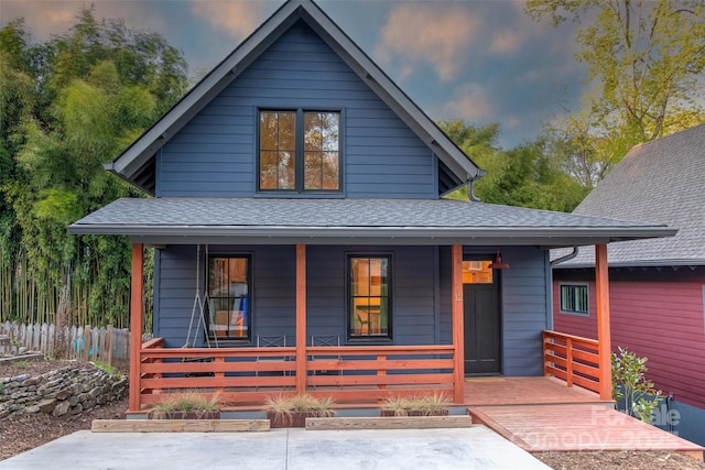 view of front of home with a porch, a shingled roof, and fence