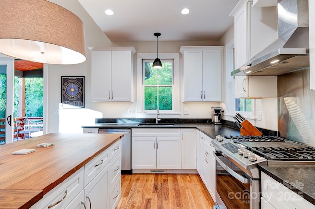 kitchen featuring butcher block counters, stainless steel appliances, wall chimney range hood, white cabinetry, and a sink