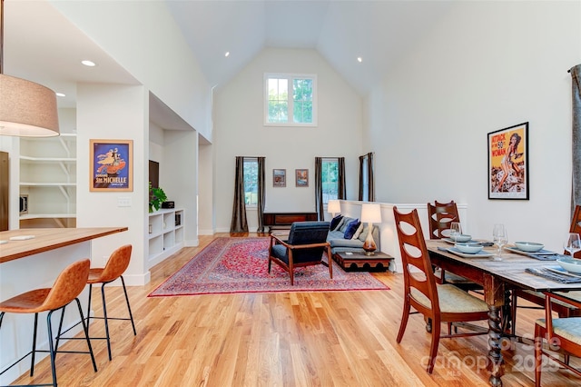 dining room with light wood-style flooring, built in shelves, high vaulted ceiling, and baseboards