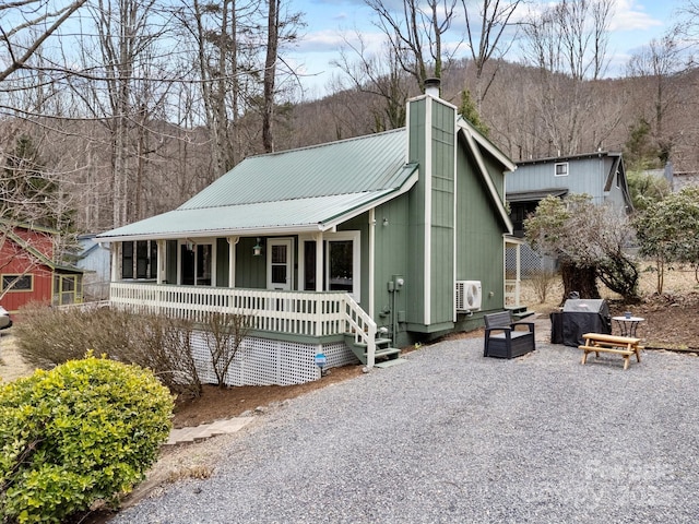 view of front of home with ac unit, a porch, a chimney, and metal roof