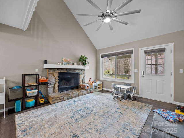 living area featuring baseboards, a stone fireplace, wood finished floors, high vaulted ceiling, and a ceiling fan