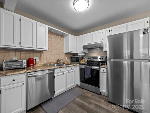 kitchen with under cabinet range hood, a toaster, appliances with stainless steel finishes, white cabinetry, and a sink