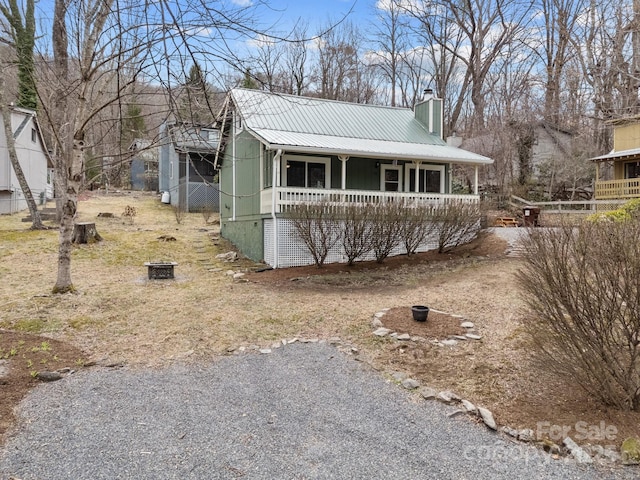 view of front of house featuring metal roof, covered porch, driveway, and a chimney