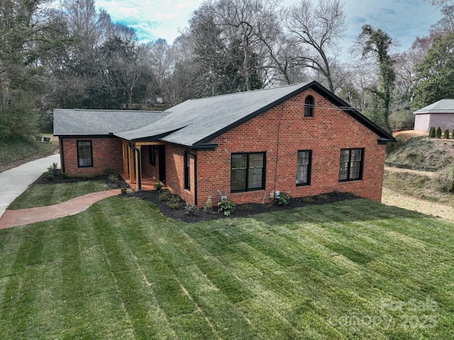 view of front of home with roof with shingles, a front lawn, and brick siding