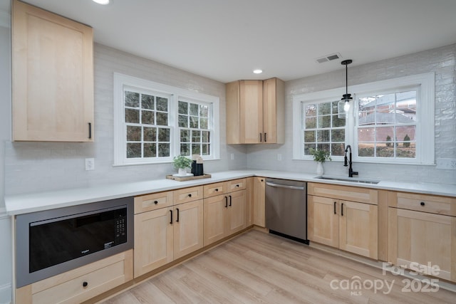 kitchen with built in microwave, dishwasher, a sink, and light brown cabinetry