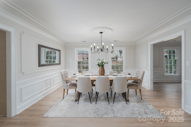 dining space with ornamental molding, light wood-type flooring, a decorative wall, and an inviting chandelier