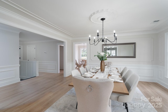 dining area with light wood-style flooring, a decorative wall, visible vents, an inviting chandelier, and crown molding