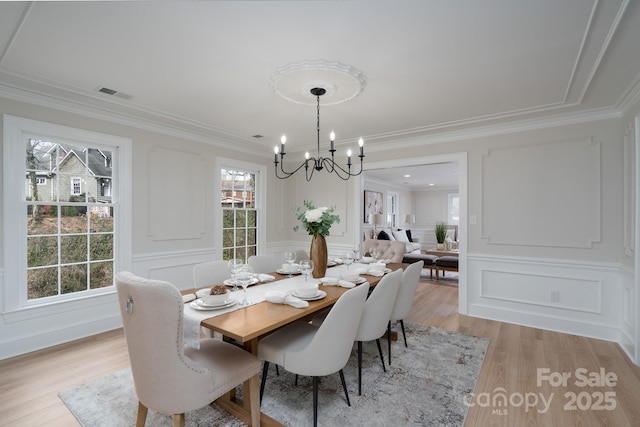 dining space featuring crown molding, visible vents, a decorative wall, light wood-style flooring, and a chandelier