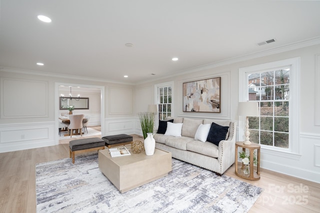 living area with recessed lighting, visible vents, a decorative wall, light wood-style flooring, and ornamental molding