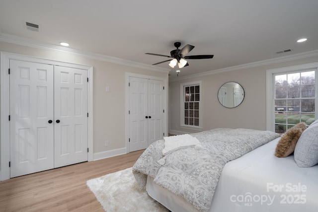 bedroom featuring multiple closets, visible vents, crown molding, and light wood-style flooring