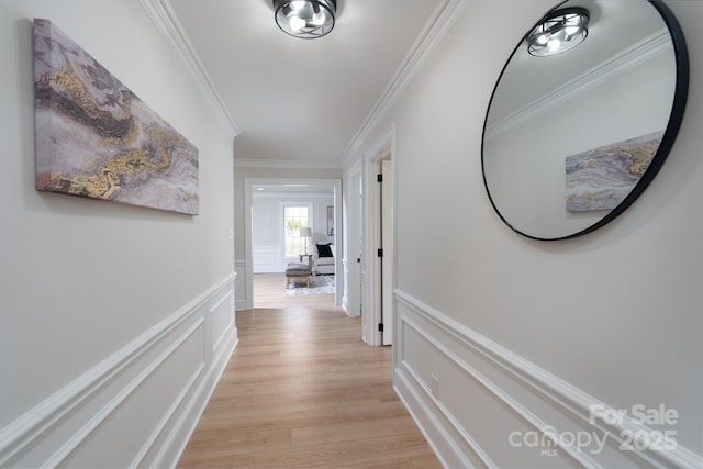 hall with light wood-style floors, ornamental molding, a decorative wall, and wainscoting