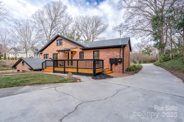 view of front of home with brick siding, a deck, and roof with shingles