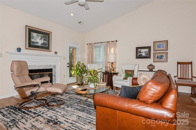 living area featuring lofted ceiling, a premium fireplace, wood finished floors, visible vents, and a ceiling fan