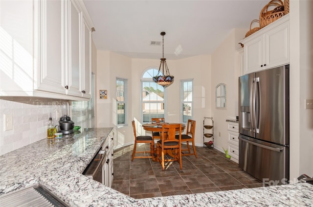 kitchen with pendant lighting, tasteful backsplash, white cabinets, light stone countertops, and stainless steel fridge with ice dispenser