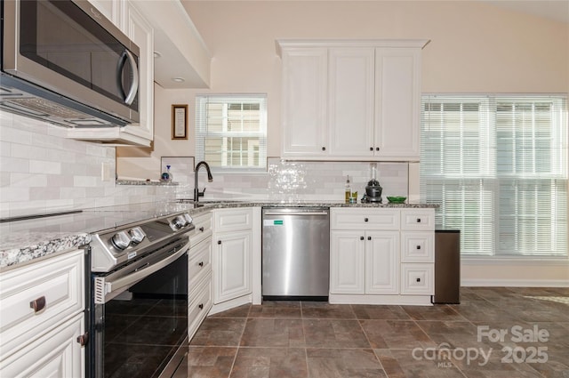 kitchen featuring appliances with stainless steel finishes, white cabinets, a sink, and light stone countertops