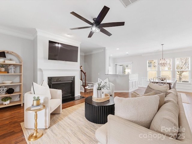 living area featuring a fireplace with flush hearth, visible vents, wood finished floors, and ornamental molding