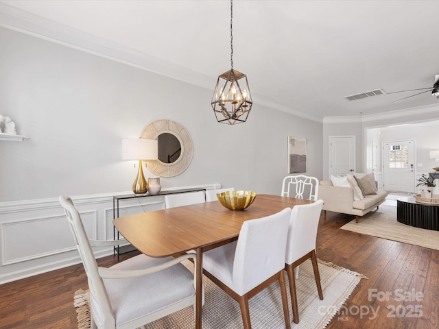 dining area with visible vents, dark wood finished floors, a wainscoted wall, ceiling fan, and crown molding