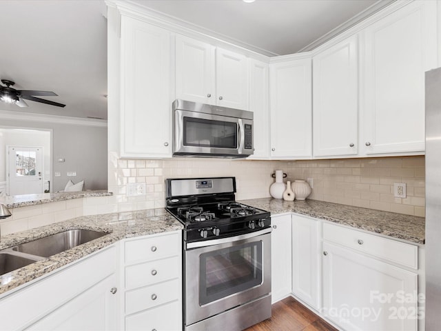 kitchen featuring backsplash, appliances with stainless steel finishes, white cabinets, a sink, and light stone countertops