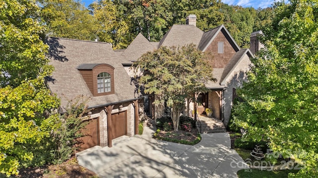 view of front of house featuring driveway, a shingled roof, a chimney, and a garage