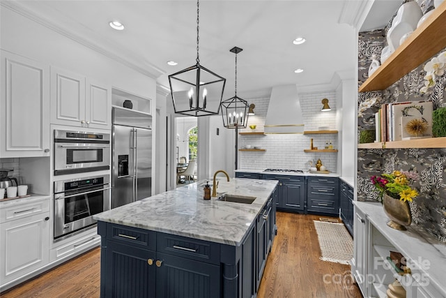 kitchen with open shelves, appliances with stainless steel finishes, white cabinets, a sink, and wall chimney range hood