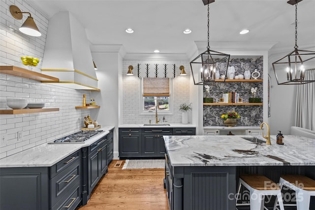 kitchen featuring ventilation hood, light wood-type flooring, stainless steel gas cooktop, open shelves, and a sink