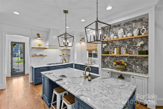 kitchen with blue cabinets, premium range hood, open shelves, and a sink