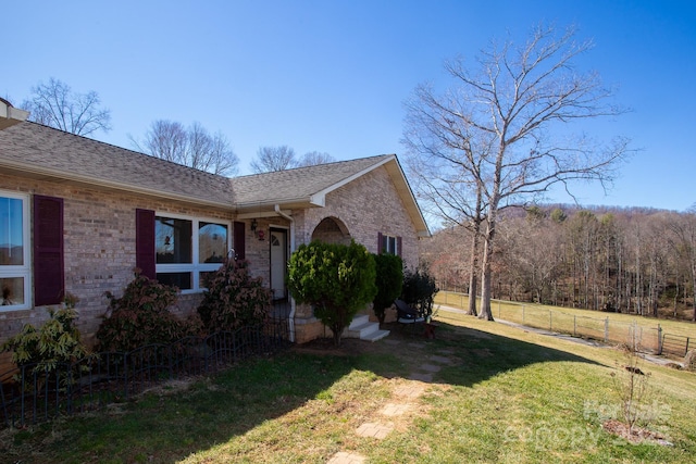 exterior space with brick siding, roof with shingles, a front yard, and fence