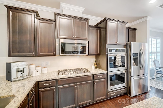 kitchen with dark brown cabinets, appliances with stainless steel finishes, ornamental molding, and dark wood finished floors