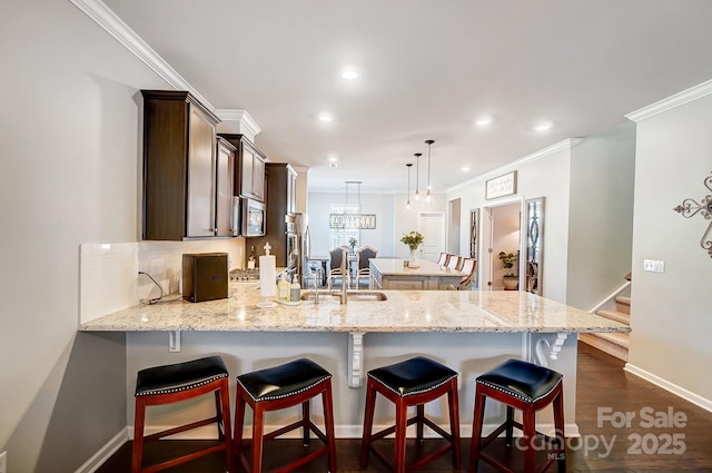 kitchen with tasteful backsplash, stainless steel microwave, dark brown cabinets, crown molding, and a peninsula