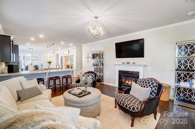 living room featuring a glass covered fireplace, crown molding, dark wood-style flooring, and an inviting chandelier