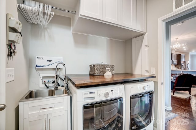 washroom with wood finished floors, visible vents, cabinet space, a sink, and washing machine and dryer