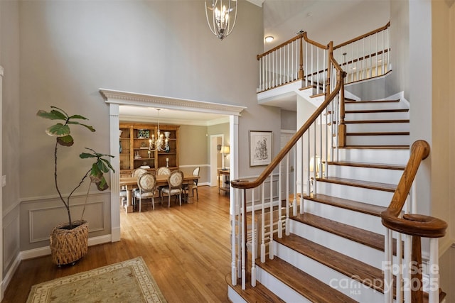 staircase with a chandelier, a decorative wall, a towering ceiling, and wood finished floors