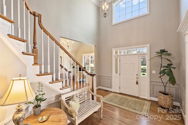 foyer featuring a chandelier, a decorative wall, a wainscoted wall, wood finished floors, and stairway