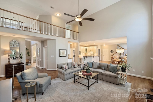 living room with ceiling fan with notable chandelier, stairway, wood finished floors, and baseboards