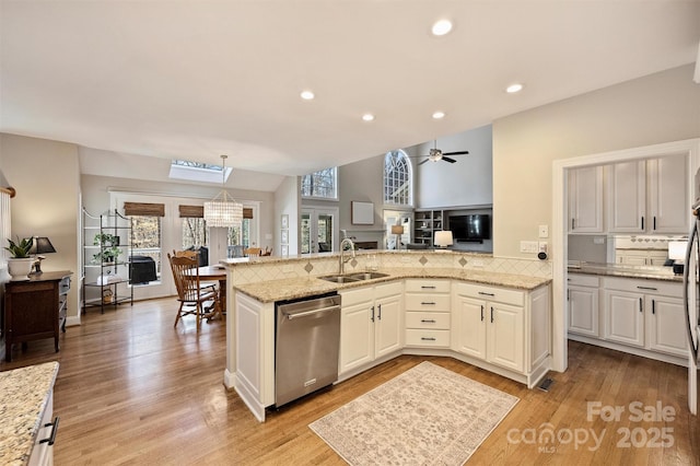 kitchen featuring dishwasher, open floor plan, a peninsula, light wood-style floors, and a sink