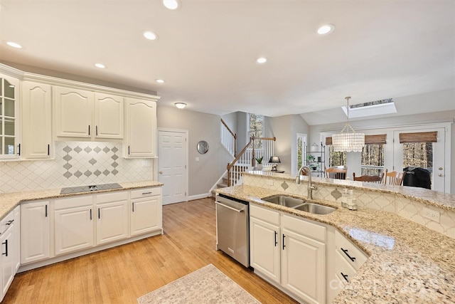 kitchen featuring glass insert cabinets, black electric cooktop, stainless steel dishwasher, light wood-style floors, and a sink