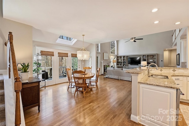 dining space featuring light wood-style floors, recessed lighting, vaulted ceiling with skylight, and ceiling fan with notable chandelier