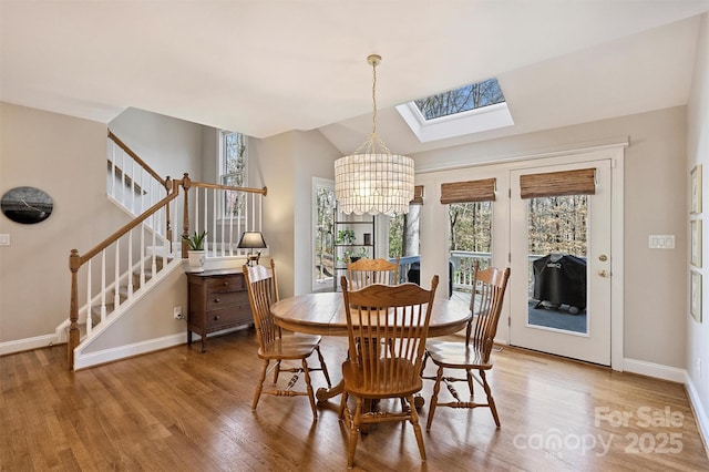 dining space with vaulted ceiling with skylight, stairs, light wood-style flooring, and a notable chandelier