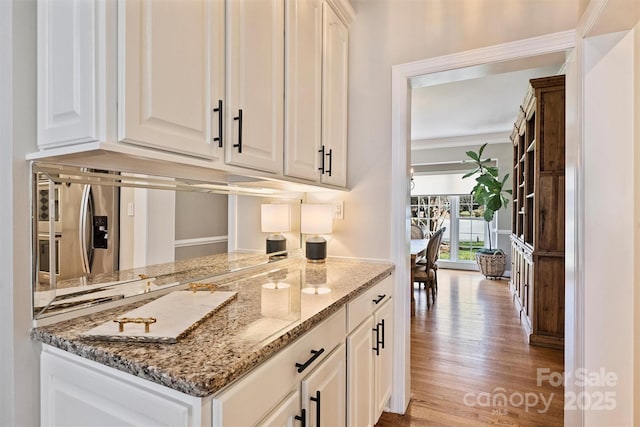 kitchen featuring light stone counters, crown molding, light wood-style floors, white cabinetry, and stainless steel fridge with ice dispenser