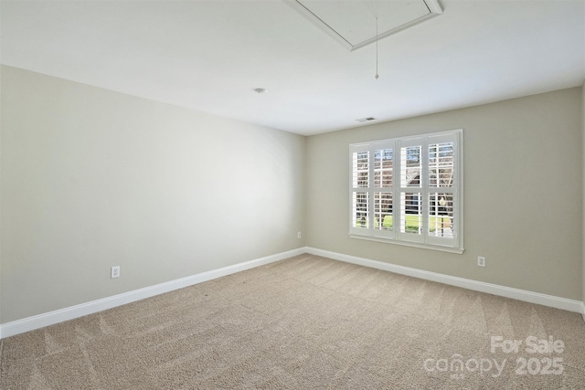 empty room featuring attic access, carpet flooring, and baseboards