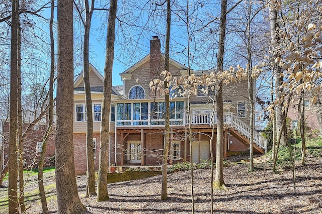 rear view of property with a deck, brick siding, a sunroom, stairway, and a chimney